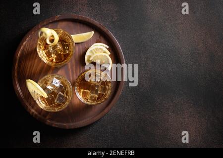 Drei Gläser Whiskey serviert auf Felsen mit Zitrone für festliche Party auf braunem Hintergrund. Speicherplatz kopieren. Blick von oben. Stockfoto