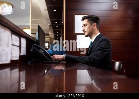 Hotelrezeption, die seine Verantwortung wahrnimmt und die Gäste und deren Verwaltung übernimmt Fragen Stockfoto