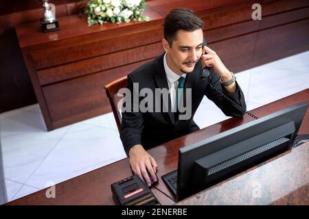 Rezeptionist in schwarzem Anzug sitzen und arbeiten, Rezeptionskonzept Stockfoto
