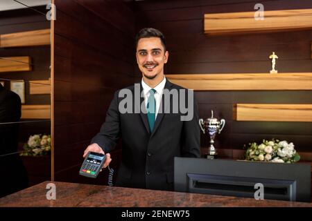 Der Rezeptionist hält mit der rechten Hand einen Kreditkartenleser Stockfoto