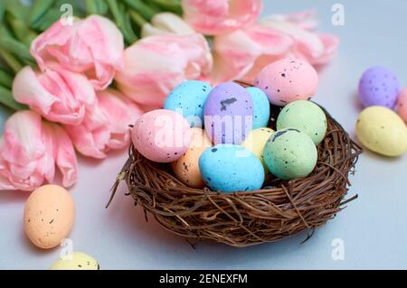 Schöne rosa Tulpen mit bunten Wachteleiern in einem Nest auf einem hellgrauen Steingrund. Frühling und Osterferien Konzept Stockfoto