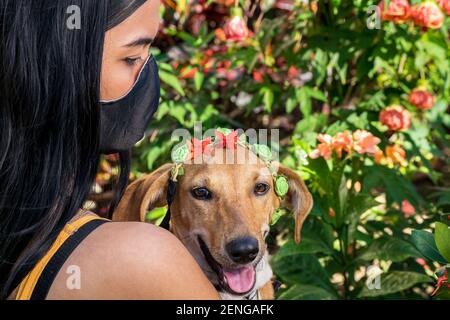 Nahaufnahme eines kubanischen Mädchens, das eine schwarze Maske trägt Sie hält ihre Hündin im Garten nahe bei sich Stockfoto