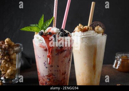 Zwei köstliche Beerenmilchshake garniert mit Schlagsahne, Heidelbeeren, tropfender Marmelade auf dunklem Hintergrund. Nahaufnahme. Stockfoto