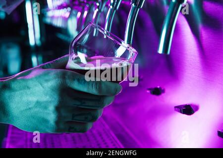 Nahaufnahme männliche Hand mit Glas Gießen Bier vom Fass zu Glas in Neonlicht. Stockfoto