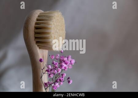 Gesichtsmassagebürste mit natürlichen Borsten auf Leinenhintergrund mit rosa und getrockneten Blumen. Umweltfreundliches Kosmetikkonzept. Stockfoto