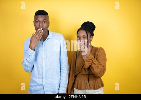 Junges afroamerikanisches Paar, das über gelbem Hintergrund den Mund mit der Hand bedeckt, schockiert und Angst vor Fehlern. Überraschter Ausdruck Stockfoto