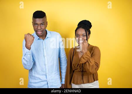 Junges afroamerikanisches Paar, das über gelbem Hintergrund wütend und wütend steht, die Faust frustriert und wütend aufhebt, während es vor Wut schreit. Rage und ag Stockfoto
