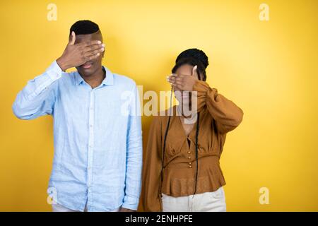 Junge afroamerikanische Paar steht über gelben Hintergrund ernst und Ihre Augen mit Händen bedecken Stockfoto