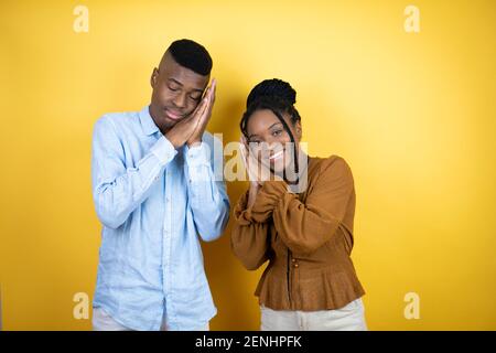 Junges afroamerikanisches Paar, das über gelbem Hintergrund schläft müde träumend und posiert mit den Händen zusammen, während lächelnd mit geschlossenen Augen. Stockfoto