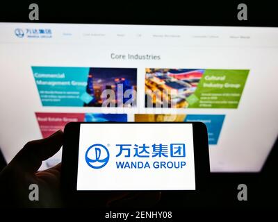 High-Angle-Ansicht der Person hält Handy mit Logo des chinesischen Konglomerats Wanda Group auf dem Bildschirm vor der Webseite. Konzentrieren Sie sich auf die Telefonanzeige. Stockfoto