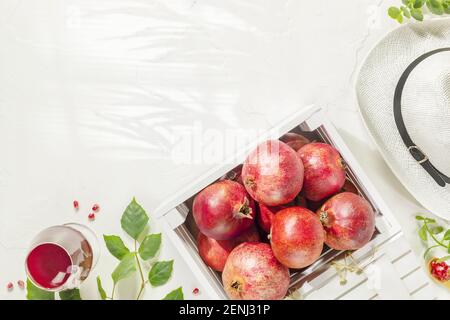 Frische, reife Granatäpfel mit Blättern in einer Holzkiste und Glas frischen Granatapfelsaft auf weißem Hintergrund mit Kopierfläche. Gesunde Früchte der Saison Stockfoto