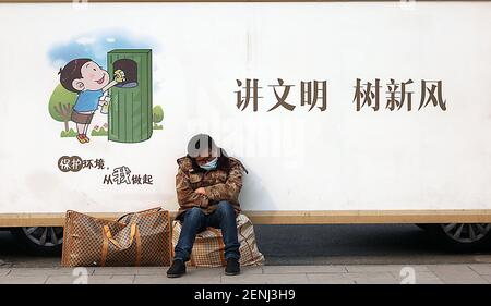 Peking, China. Februar 2021, 26th. Ein Chinese sitzt auf seinem Gepäck an einer Fernbusstation neben einem Transparent, das sich für einen guten Bürger in der Innenstadt von Peking am Freitag, dem 26. Februar 2021, wirbt. Chinas Präsident Xi Jinping behauptete im vergangenen Jahr, dass es ein langfristiges Ziel erreicht habe, alle Menschen aus extremer Armut zu befreien. Foto von Stephen Shaver/UPI Kredit: UPI/Alamy Live Nachrichten Stockfoto