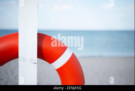 An einem weißen Pfosten an einem Sandstrand hängt eine orangefarbene Rettungsboje. Meereshorizont und Kopierraum für Text. Stockfoto