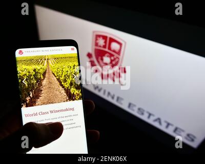 Person hält Handy mit Website der australischen Firma Treasury Wine Estates auf dem Bildschirm vor dem Logo. Fokus auf der Mitte des Telefondisplays. Stockfoto