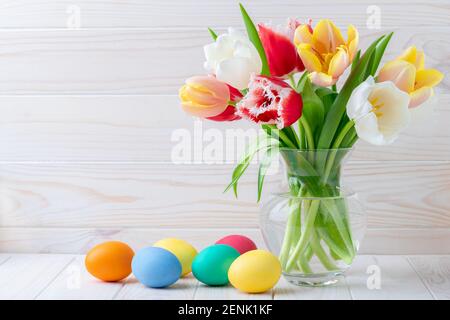 Ostereier und ein Strauß Tulpen auf einem Holztisch, florales Stillleben. Urlaubskonzept. Grußkarte mit Kopierplatz, leerer Platz für Text. Fest Stockfoto