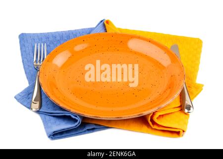 Orangefarbener leerer Teller mit Messer und Gabel auf blauen und gelben Baumwollhandtüchern isoliert auf weißem Hintergrund. Stockfoto