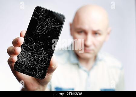 Telefon mit EINEM defekten Bildschirm Nahaufnahme. Ein weißer Mann hält ein schwarzes Smartphone mit einem geknackten Display. Stockfoto
