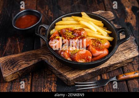 Currywurst Würste mit Curry Gewürz auf Würsten serviert Pommes in einer Pfanne. Dunkler Holzhintergrund. Draufsicht Stockfoto