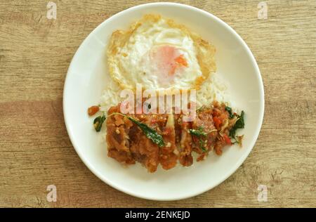 Würzig gebratenes knuspriges Huhn mit Basilikumblättern und Chili-Belag Ei auf Reis auf dem Teller Stockfoto