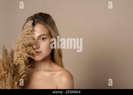 Schöne junge weibliche Modell mit lockeren Haaren hält trockene Pampas Gras in ihren Händen. Das Konzept der Naturkosmetik aus Weizenkörnern. Hautpflege. Stockfoto