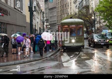 Passagiere drängen sich unter farbenfrohen Regenschirmen, während sie an einem regnerischen Tag auf der belebten Canal Street an Bord der legendären New Orleans Straßenbahn gehen. Stockfoto