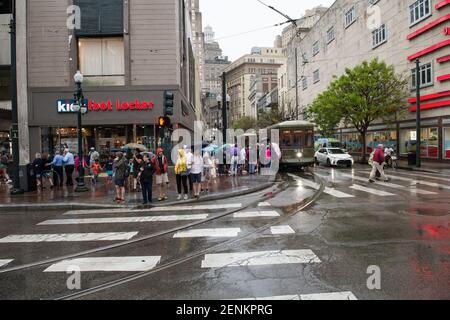 Passagiere drängen sich unter farbenfrohen Regenschirmen, während sie an einem regnerischen Tag auf der belebten Canal Street an Bord der legendären New Orleans Straßenbahn gehen. Stockfoto