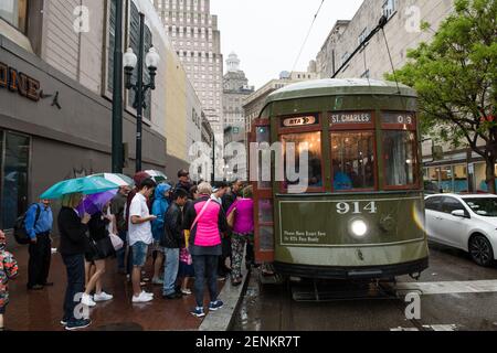 Passagiere drängen sich unter farbenfrohen Regenschirmen, während sie an einem regnerischen Tag auf der belebten Canal Street an Bord der legendären New Orleans Straßenbahn gehen. Stockfoto