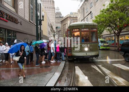 Passagiere drängen sich unter farbenfrohen Regenschirmen, während sie an einem regnerischen Tag auf der belebten Canal Street an Bord der legendären New Orleans Straßenbahn gehen. Stockfoto