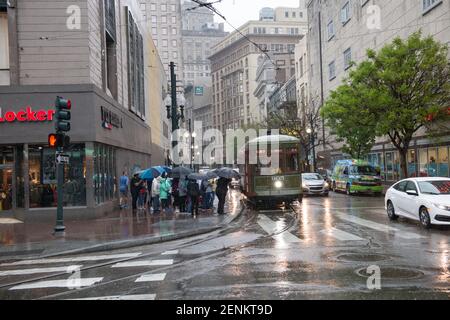 Passagiere drängen sich unter farbenfrohen Regenschirmen, während sie an einem regnerischen Tag auf der belebten Canal Street an Bord der legendären New Orleans Straßenbahn gehen. Stockfoto