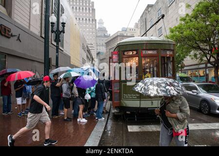 Passagiere drängen sich unter farbenfrohen Regenschirmen, während sie an einem regnerischen Tag auf der belebten Canal Street an Bord der legendären New Orleans Straßenbahn gehen. Stockfoto