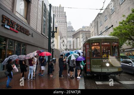 Passagiere drängen sich unter farbenfrohen Regenschirmen, während sie an einem regnerischen Tag auf der belebten Canal Street an Bord der legendären New Orleans Straßenbahn gehen. Stockfoto