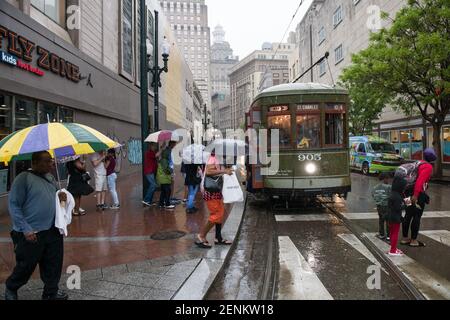 Passagiere drängen sich unter farbenfrohen Regenschirmen, während sie an einem regnerischen Tag auf der belebten Canal Street an Bord der legendären New Orleans Straßenbahn gehen. Stockfoto