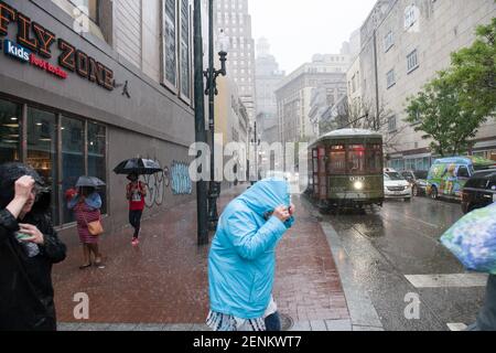 Passagiere drängen sich unter farbenfrohen Regenschirmen, während sie an einem regnerischen Tag auf der belebten Canal Street an Bord der legendären New Orleans Straßenbahn gehen. Stockfoto