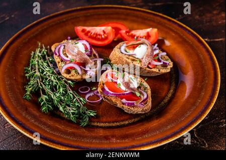 Spanische Tapas auf Brot mit Olivenöl, Kräutern, Tomaten und würzigen Sardellenfilets. Dunkler Hintergrund. Draufsicht Stockfoto