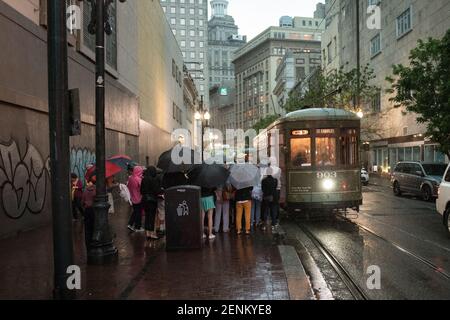 Passagiere drängen sich unter farbenfrohen Regenschirmen, während sie an einem regnerischen Tag auf der belebten Canal Street an Bord der legendären New Orleans Straßenbahn gehen. Stockfoto