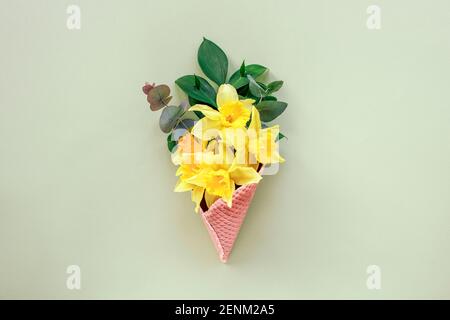 Bouquet von gelben Narzissen in einem Waffelbecher hellgrünen Hintergrund. Federkonzept. Draufsicht, flach liegend. Stockfoto