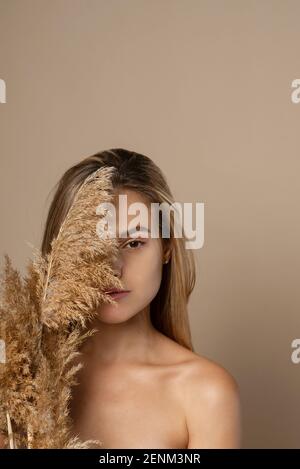 Schöne junge weibliche Modell mit lockeren Haaren hält trockene Pampas Gras in ihren Händen. Das Konzept der Naturkosmetik aus Weizenkörnern. Hautpflege. Stockfoto