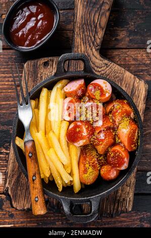 Currywurst Würste mit Curry Gewürz auf Würsten serviert Pommes in einer Pfanne. Dunkler Holzhintergrund. Draufsicht Stockfoto