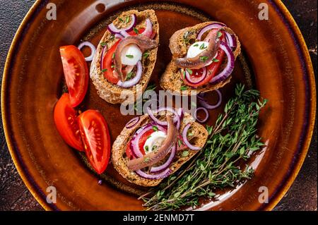 Spanische Tapas auf Brot mit Olivenöl, Kräutern, Tomaten und würzigen Sardellenfilets. Dunkler Hintergrund. Draufsicht Stockfoto