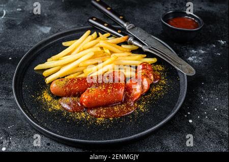 Traditionelle deutsche Currywurst, serviert mit Pommes frites. Schwarzer Hintergrund. Draufsicht Stockfoto