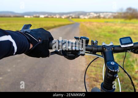Ein Fahrradlenker aus der Perspektive der ersten Person und mit einer mans Hand am Griff. Sichtbarer Fahrradcomputer und Glocke. Stockfoto