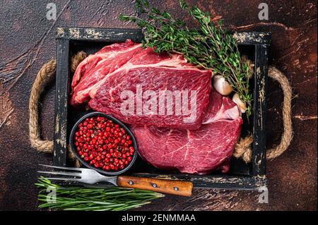 Fresh Raw Chuck Eye Roll Rindersteak in einem Holztablett mit Kräutern. Dunkler Hintergrund. Draufsicht Stockfoto