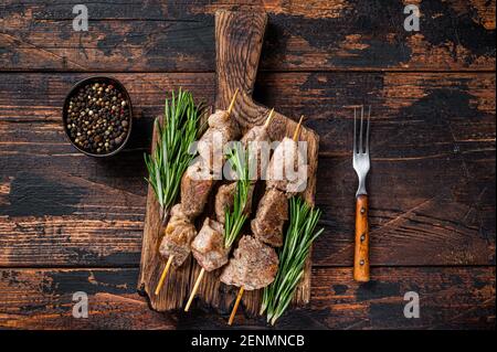 Kebab auf Spieße mit Kräutern auf einem Holzbrett. Dunkler Holzhintergrund. Draufsicht Stockfoto