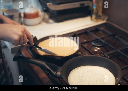 russische Frau backt Pfannkuchen in einer Pfanne Stockfoto