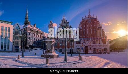 Sonnenuntergang über Schnee Rathausplatz Riga im Winter in Riga, Lettland. Blick auf das berühmte Haus der Schwarzköpfe und Rolands Statue Stockfoto