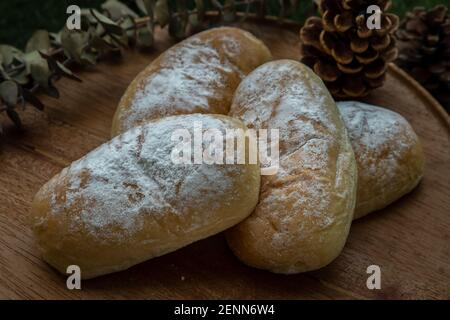 Nahaufnahme von vier hausgemachten süßen cremigen weichen Brötchen und bestreut mit Puderzucker auf runden Holzteller über rustikalem Holzboden. Bäckerei und Dessert Konz Stockfoto