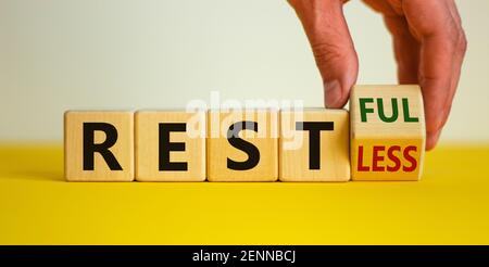 Symbol „Restless“ oder „RESTful“. Geschäftsmann dreht den Holzwürfel, ändert das Wort "stlos" in "stful". Schöner gelber Tisch, weißer Hintergrund, Polizist Stockfoto