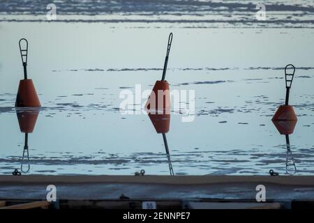 Helsinki / Finnland - 26. FEBRUAR 2021: Rote Boje, die mitten im gefrorenen See steht und Spiegelungen auf dem Wasser wirft. Stockfoto