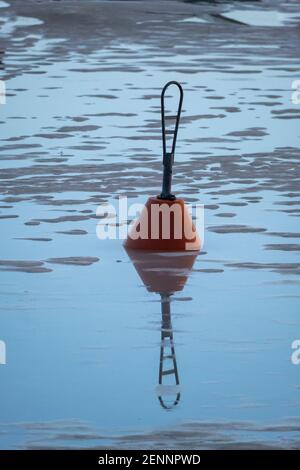 Helsinki / Finnland - 26. FEBRUAR 2021: Rote Boje, die mitten im gefrorenen See steht und Spiegelungen auf dem Wasser wirft. Stockfoto