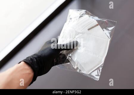 Hand in einem schützenden Gummihandschuh hält eine Packung von brandneuen KN95 medizinischen Gesichtsmasken, Kn 95 antivirale professionelle Maske geschlossen Paket, einfache Ziele Stockfoto